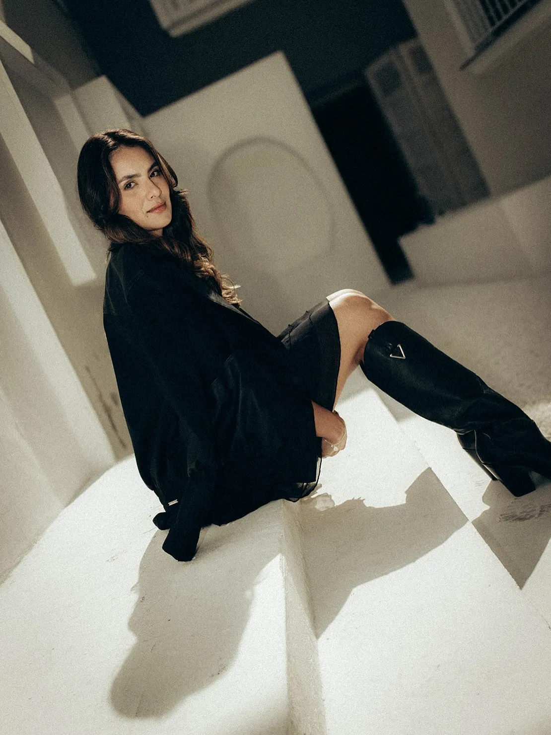 Leticia Gabriela sentada em um degrau claro, de blazer preto.